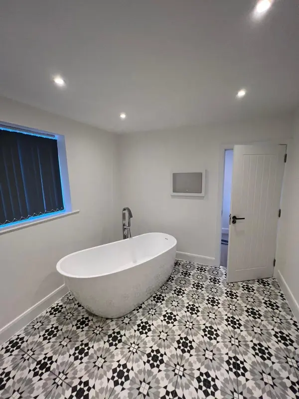 Black, grey and white patterned floor tiles around a freestanding bath