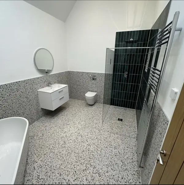 Terrazzo-effect floor and half-height wall tiles with a dark green tiled shower wall