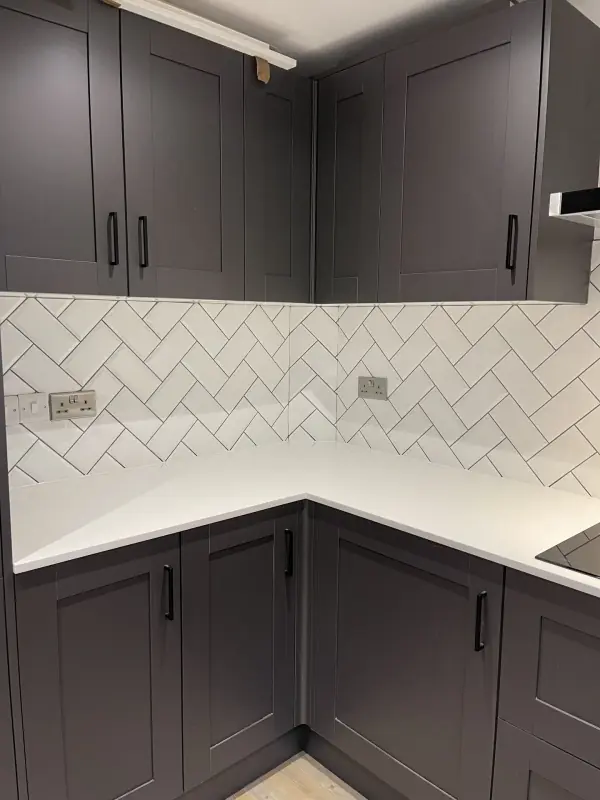 White herringbone metro tile splashback between grey kitchen units