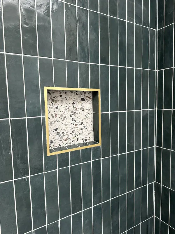 Dark green vertical stacked tiles around a brass-edged niche with a terrazzo back