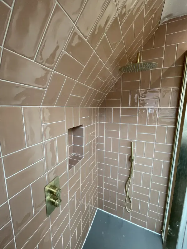 Pink gloss tiles in a shower under a sloping ceiling, with brass fittings and a tiled niche