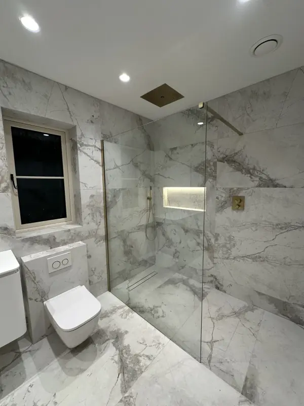 Walk-in shower in large marble-effect tiles with a lit niche and brass fittings